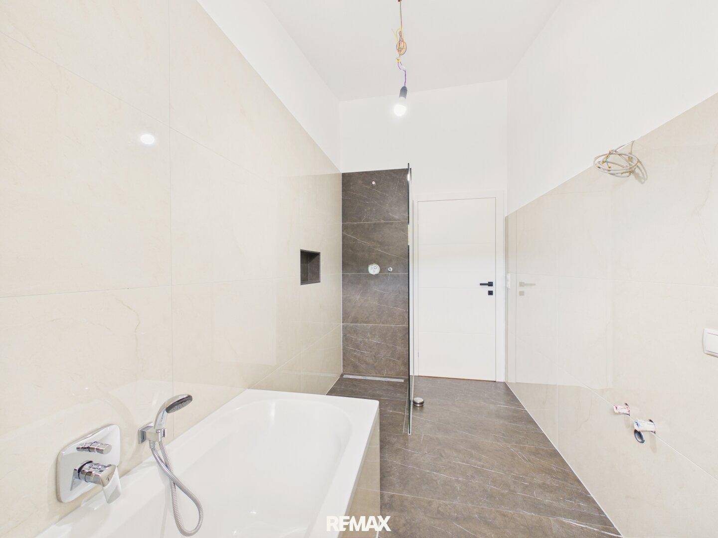 Modernes Badezimmer mit Badewanne, Dusche und großformatigen Fliesen in hellen Farbtönen.
