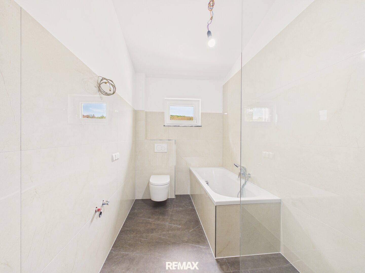 Geräumiges Badezimmer mit Badewanne, wandhängendem WC und Fenster für natürliche Belüftung.