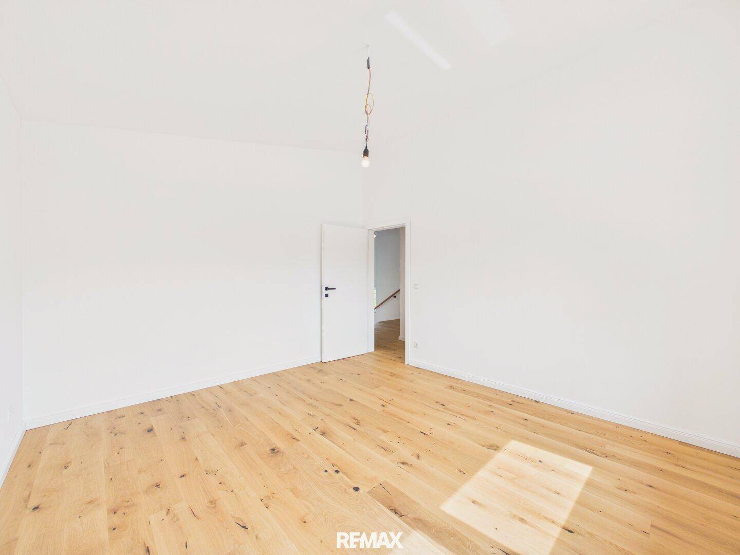 Leeres Schlafzimmer mit hellem Holzboden, weißen Wänden und natürlichem Lichteinfall.