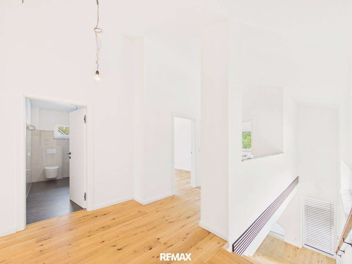Heller Flur mit Holztreppe und Blick in ein modernes Badezimmer mit Dusche.