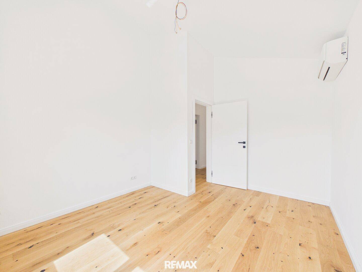 Helles Schlafzimmer mit Eichenparkettboden, weißen Wänden und Klimaanlage.