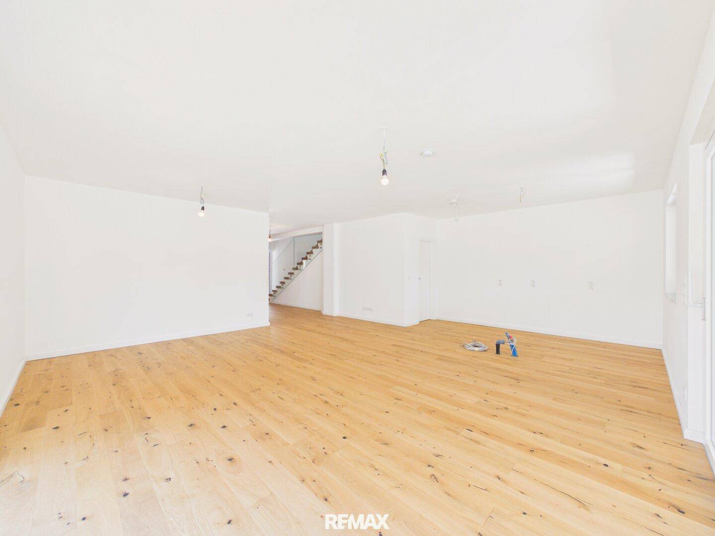 Heller, leerer Wohnraum mit neuem Holzboden, weißen Wänden und viel Tageslicht.