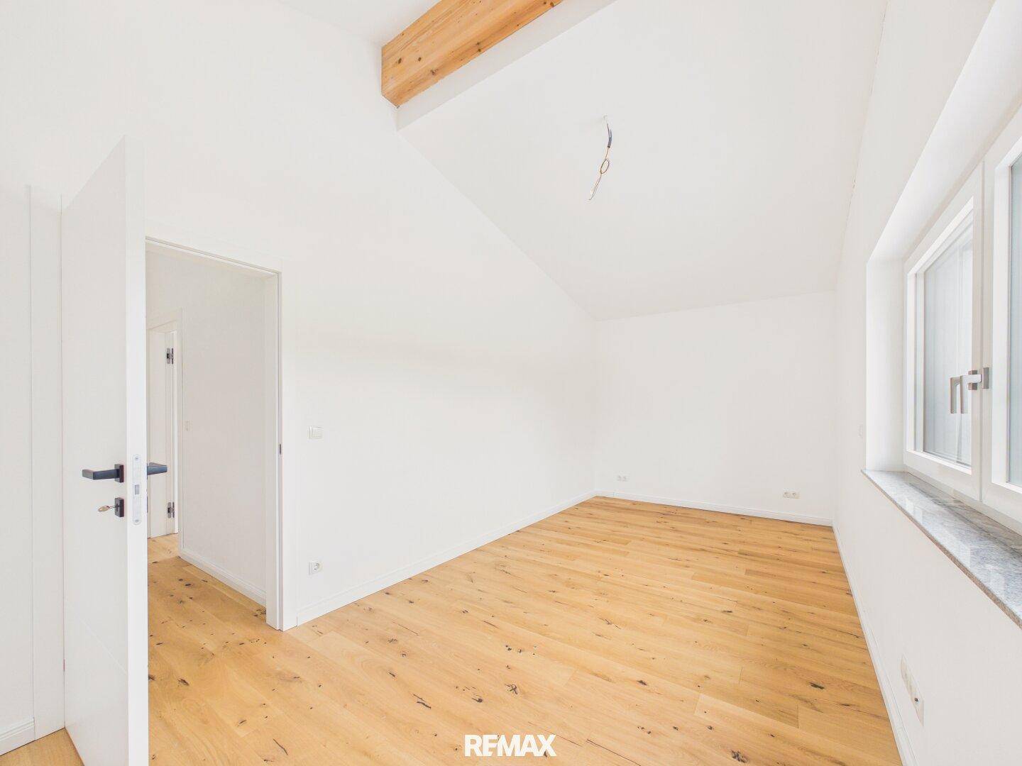 Helles Schlafzimmer im Dachgeschoss mit Holzbalken, Eichenparkett und großem Fenster.