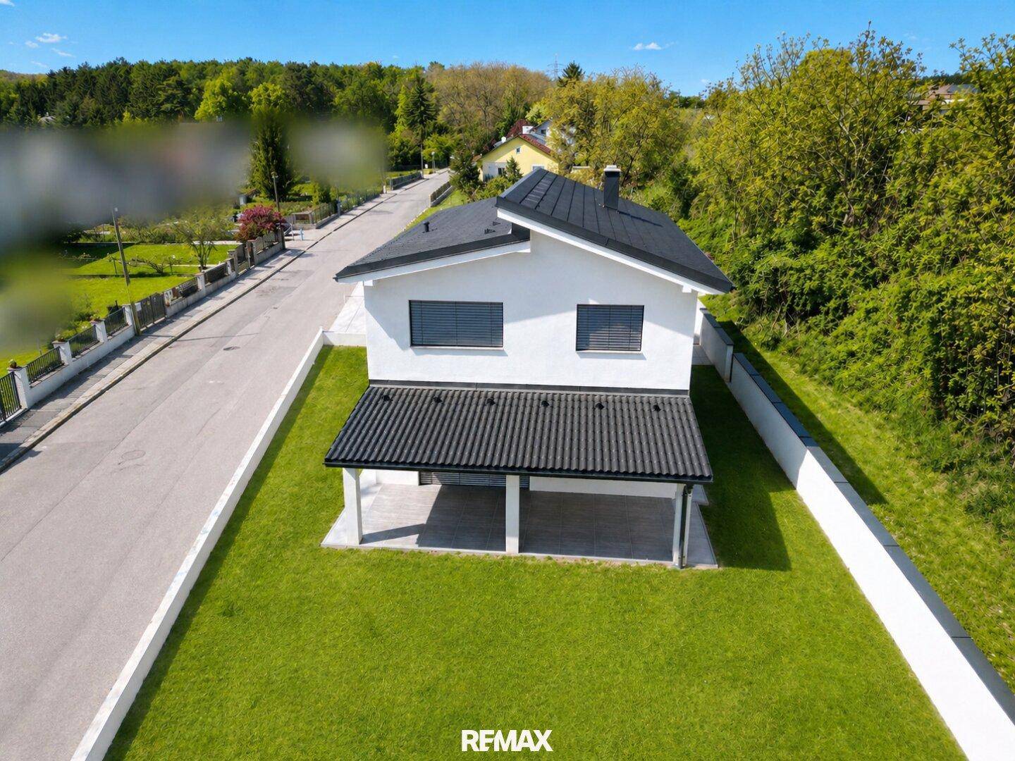 Luftaufnahme eines modernen Einfamilienhauses mit Garten und Blick auf die umliegende Wohngegend.