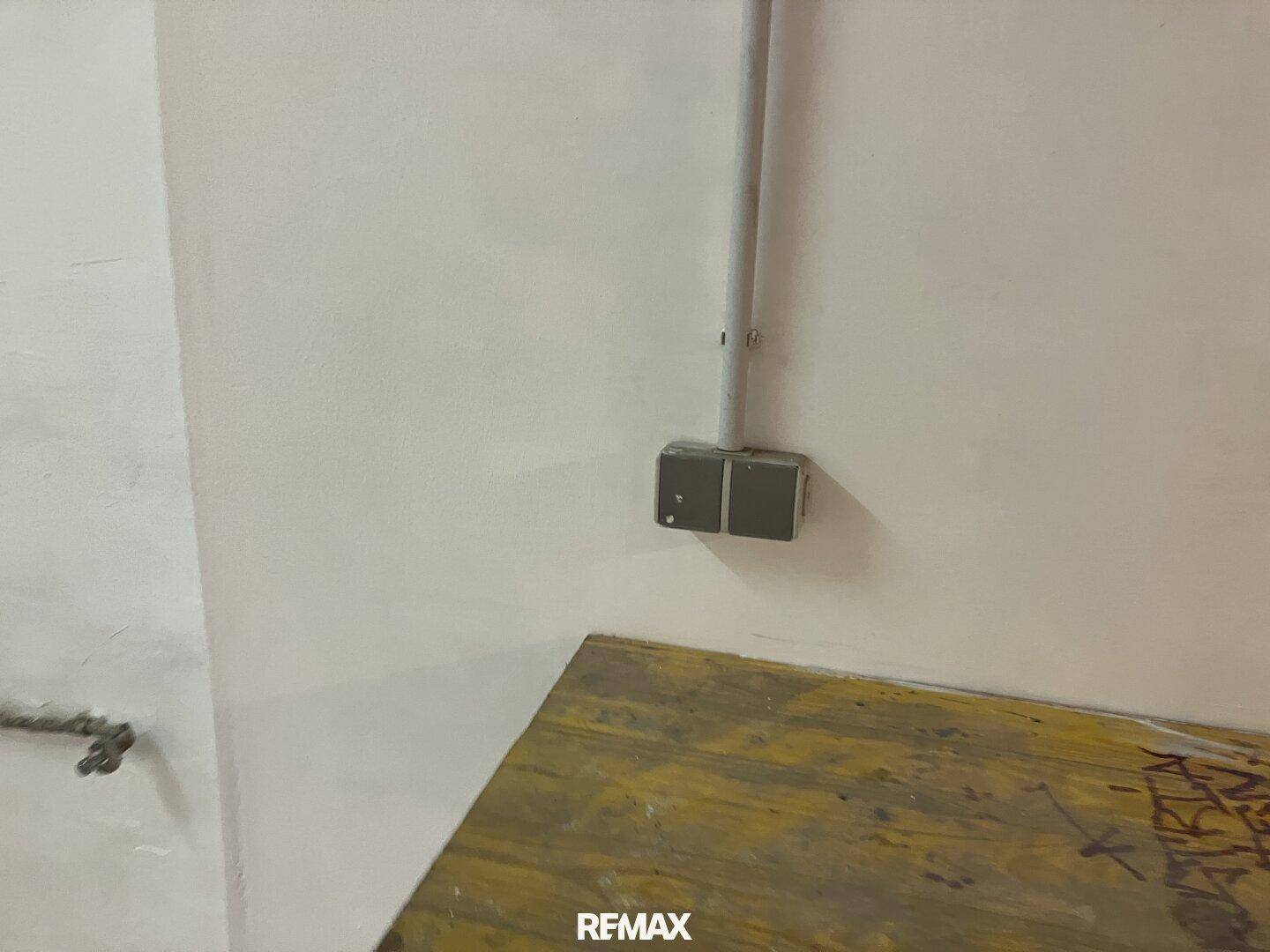 Nahaufnahme einer elektrischen Steckdose oder Anschlussdose an einer weißen Wand über einer Holzoberfläche mit sichtbarem Kabelkanal.