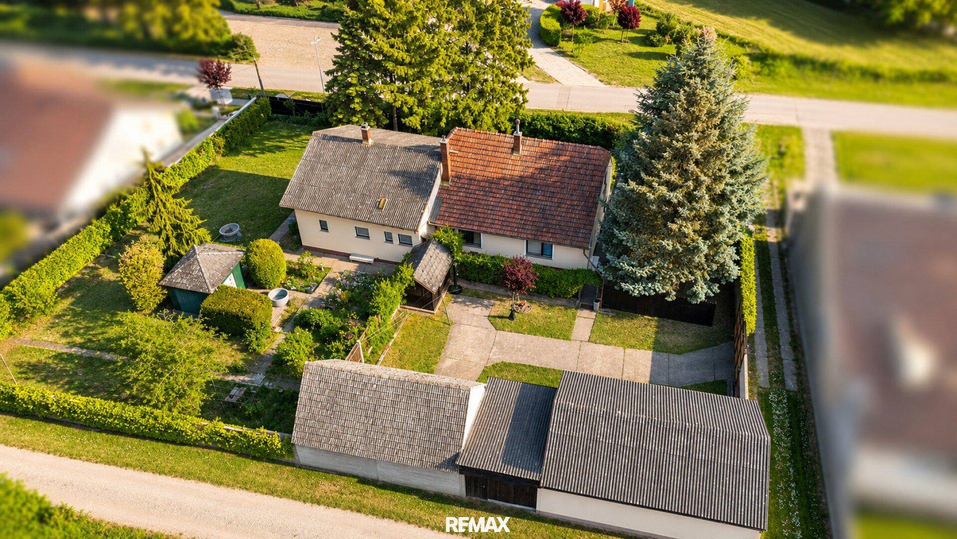 Luftaufnahme eines Einfamilienhauses mit Garten, Zufahrt und Nebengebäuden.
