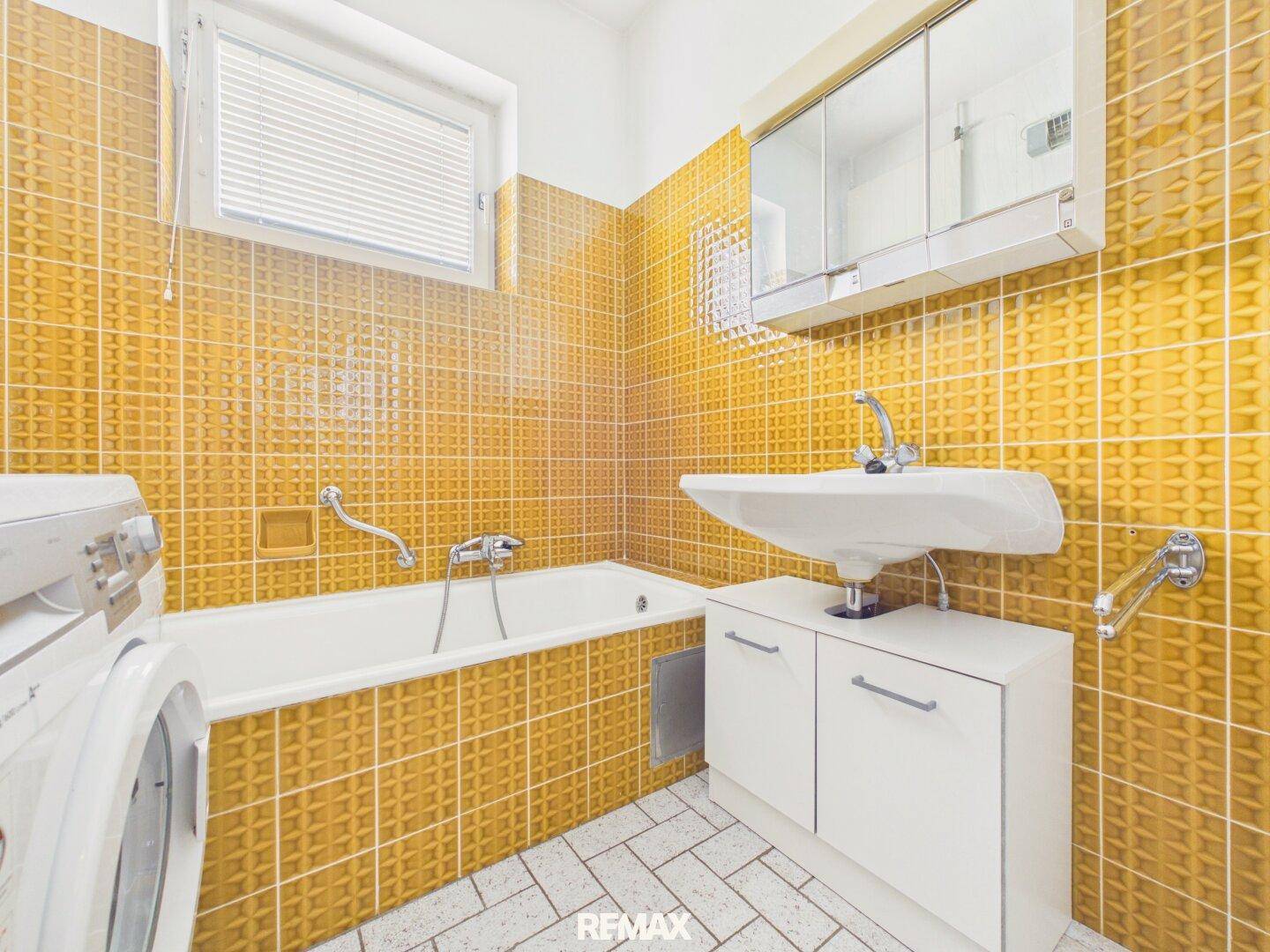 Badezimmer mit gelben Fliesen, Badewanne, Waschbecken und Fenster für Tageslicht.