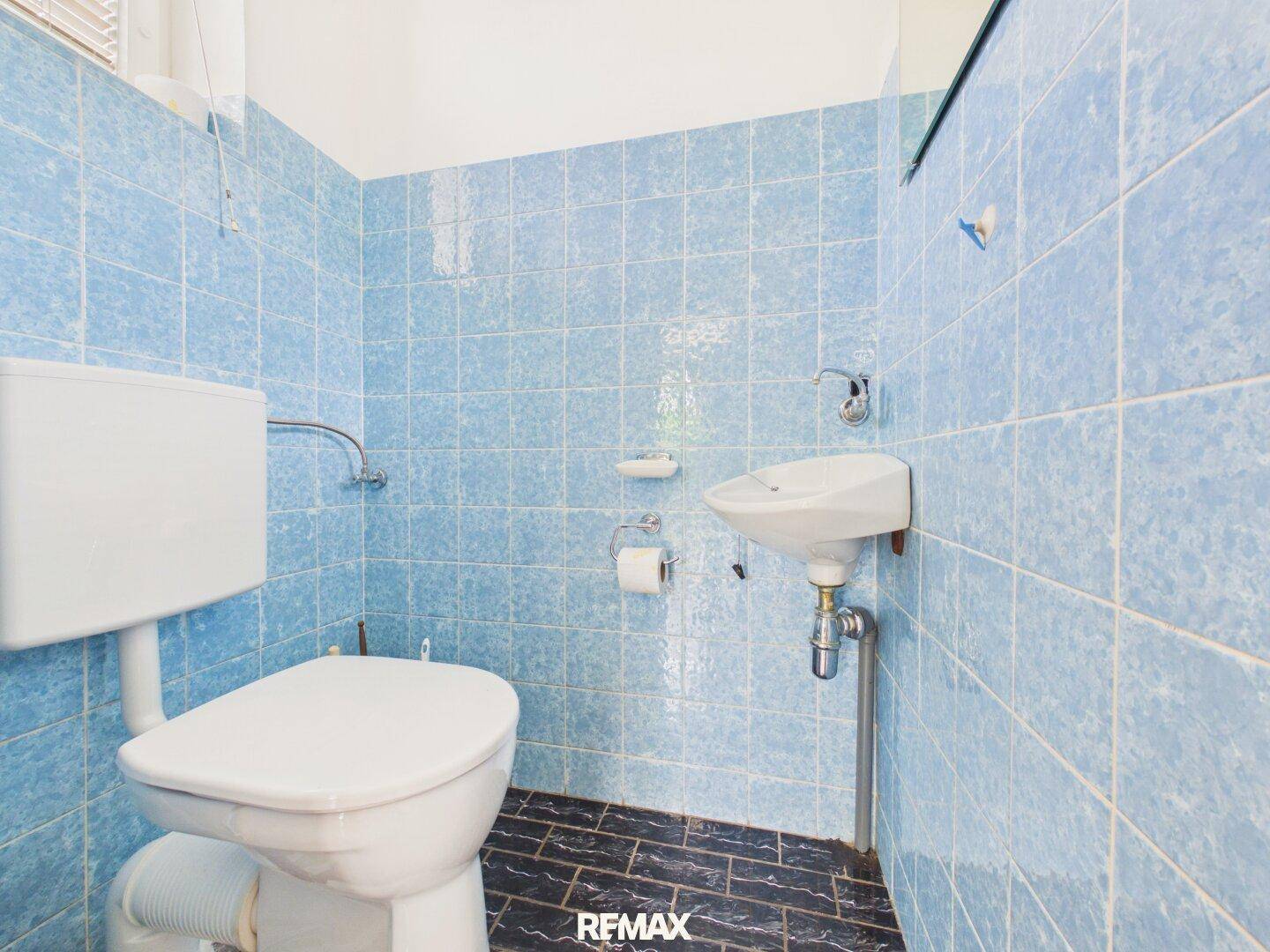 Kleines Gäste-WC mit blauen Fliesen, Toilette und Handwaschbecken.