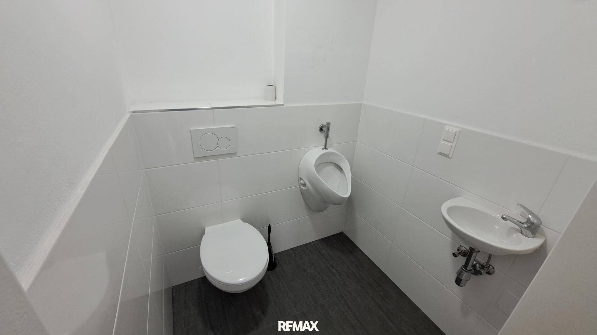 Saubere Gästetoilette mit modernem WC, Urinal und kleinem Waschbecken, in gutem Zustand.
