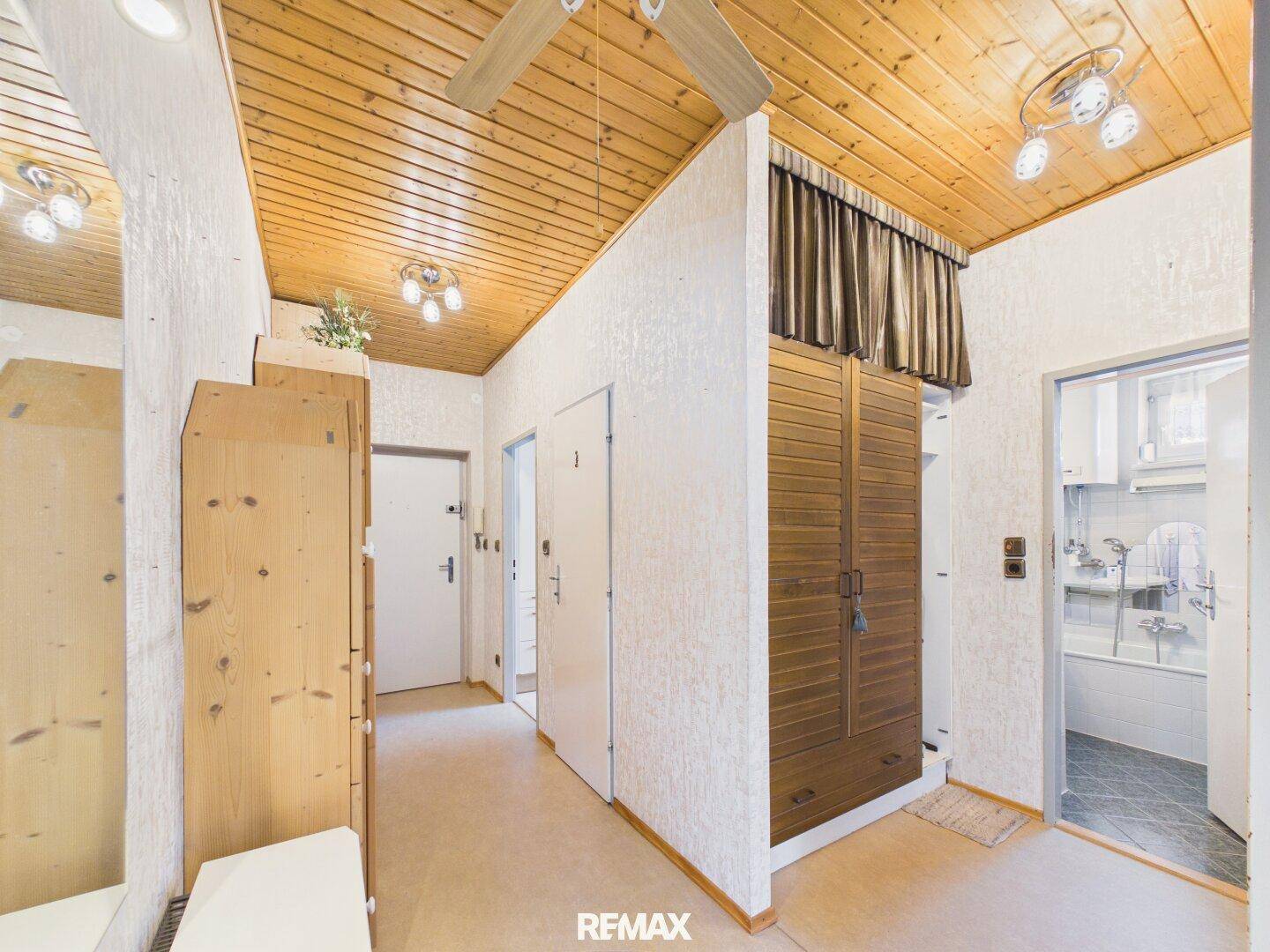 Langer Flur mit Holzdecke, Teppichboden und Einbauschränken, der zu weiteren Räumen führt.