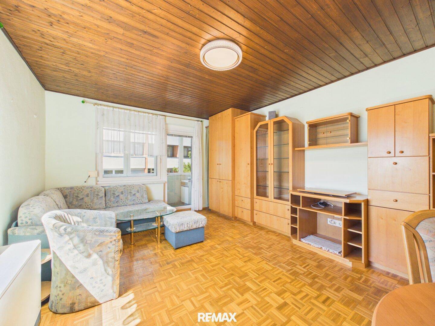 Geräumiges Wohnzimmer mit Holzdecke, Parkettboden und direktem Zugang zum Balkon.