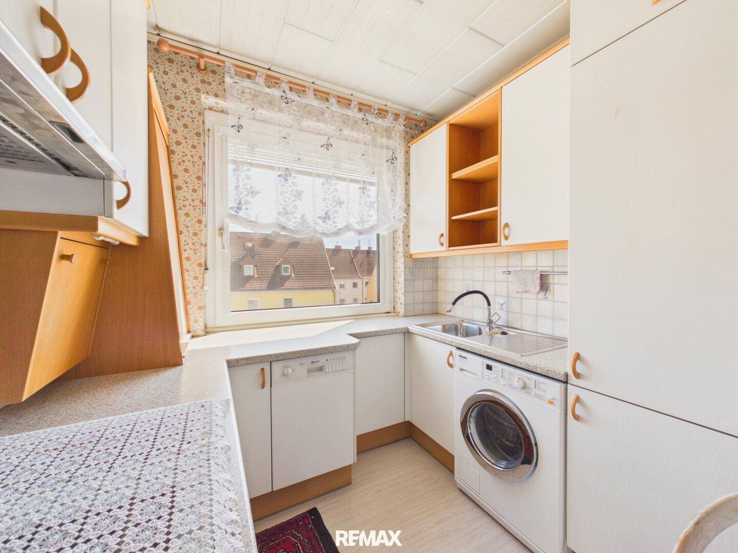 Kleine Küche mit Einbauschränken, Spüle, Geschirrspüler und Waschmaschine unter dem Fenster.