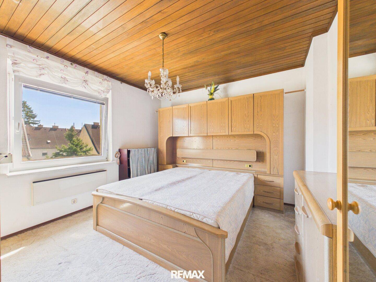 Schlafzimmer mit Holzbett, Einbauschränken und einer Holzdecke, hell durch großes Fenster.