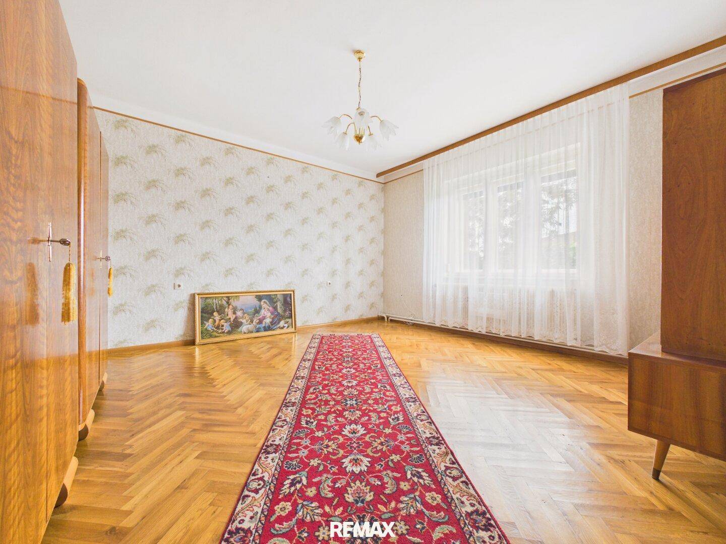 Geräumiges Schlafzimmer mit Fischgrätparkett, gemusterter Tapete und großem Fenster.