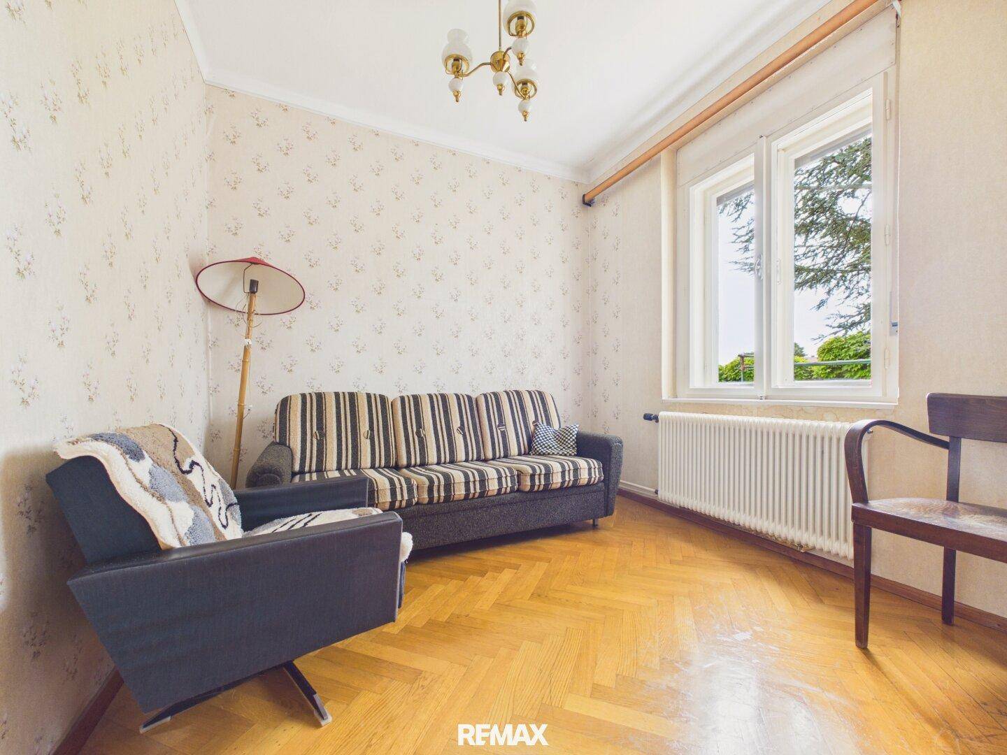 Helles Wohnzimmer mit Fischgrätparkett, gestreiftem Sofa und großem Fenster.