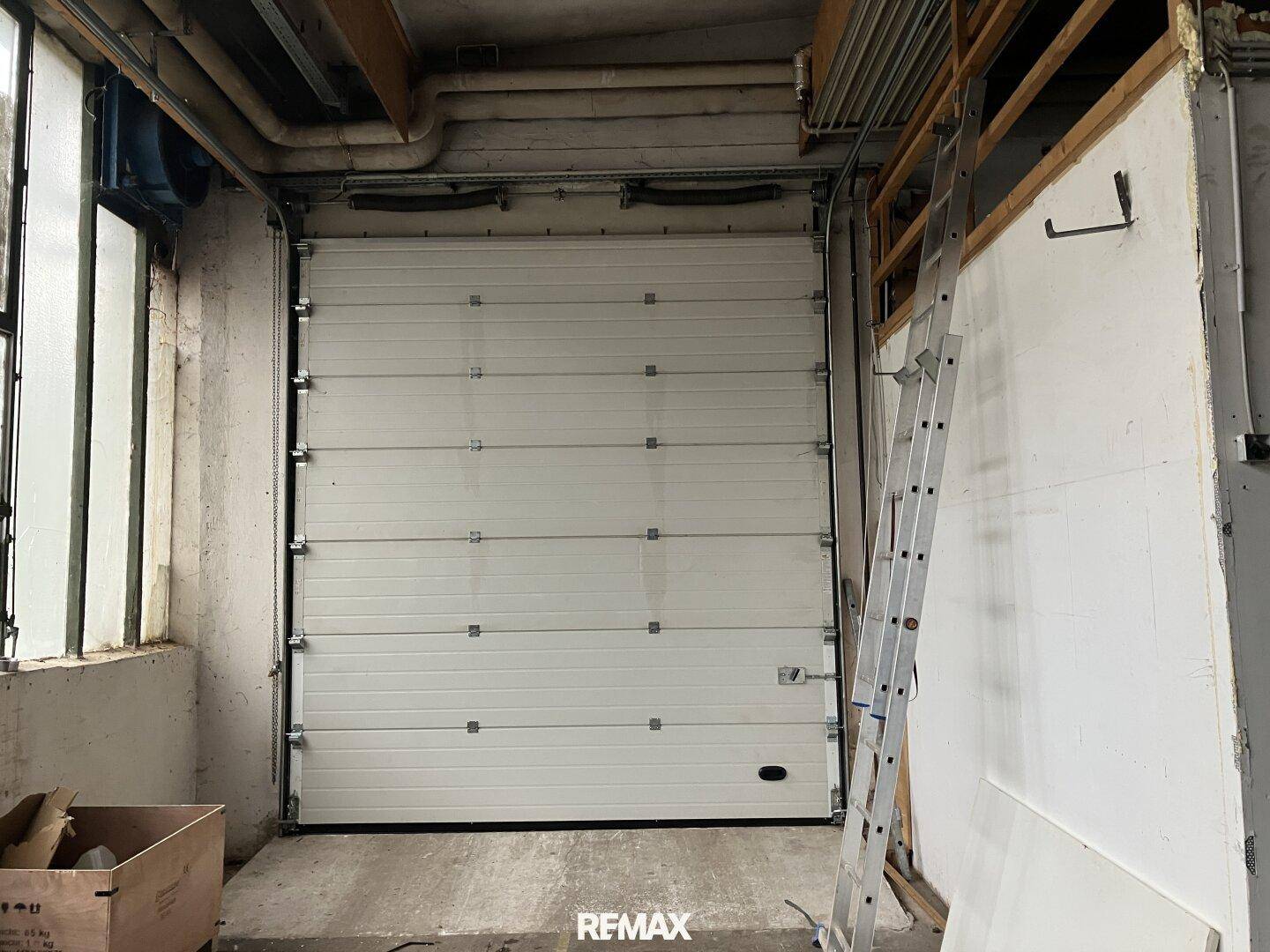Große weiße Rolltor-Einfahrt in einem Industrieraum, daneben eine Leiter an der Wand.