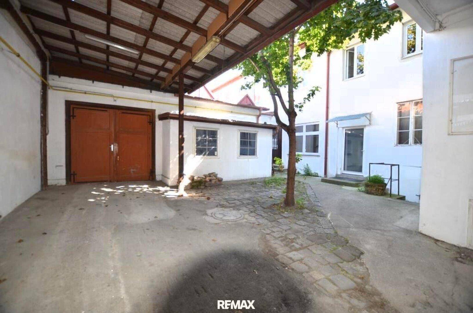 Überdachter Hofbereich mit Garagentor, Kopfsteinpflaster und einem Baum im Zentrum.