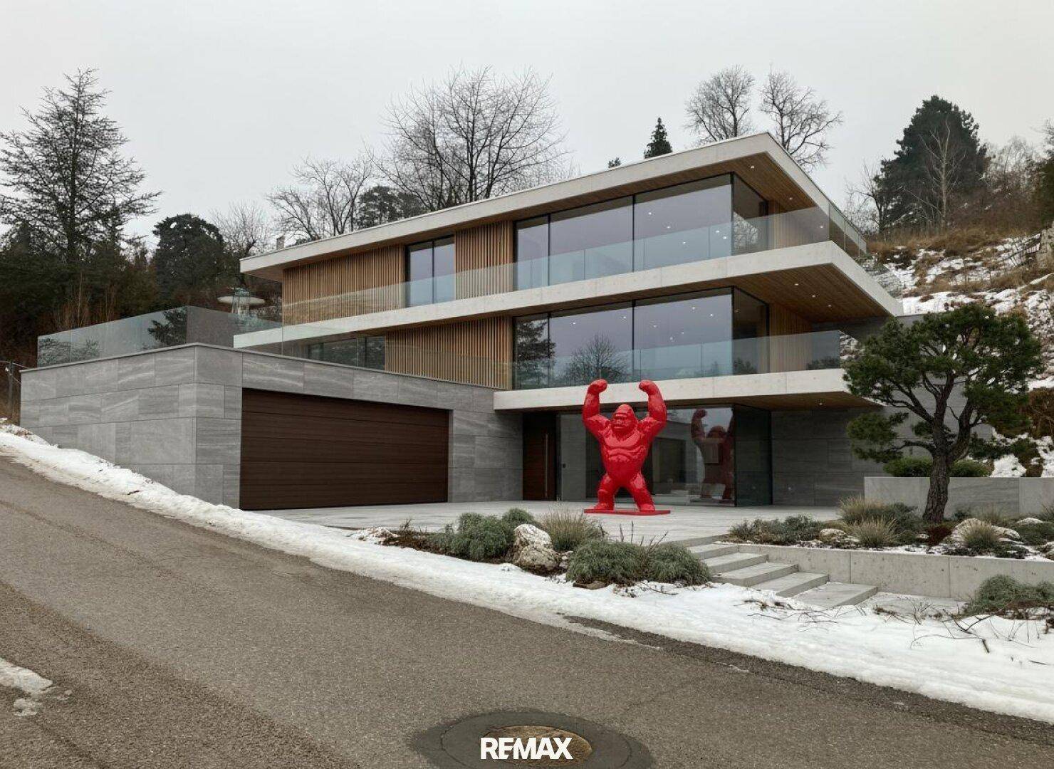Moderne Villa mit großen Glasfronten, Doppelgarage und einer auffälligen roten Gorilla-Statue im Vorgarten.