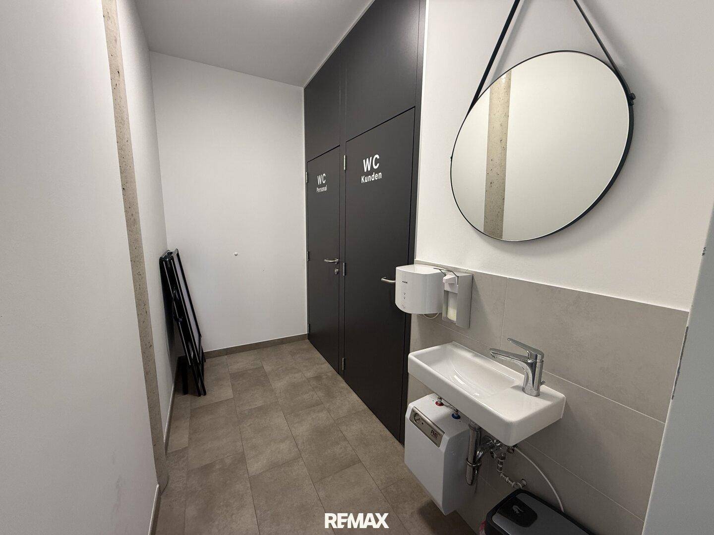 Heller Vorraum zu den Toiletten mit Waschbecken, Spiegel und zwei WC-Türen für Kunden.