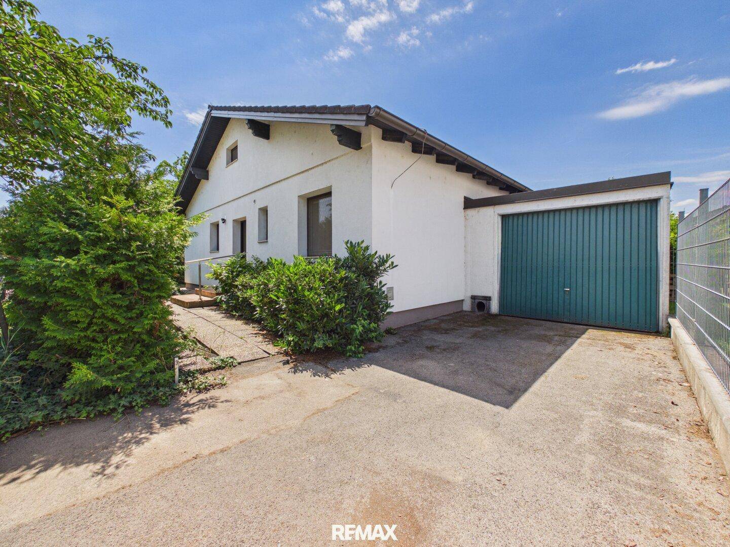Seitenansicht des Hauses mit Garage und Zufahrt unter strahlend blauem Himmel.