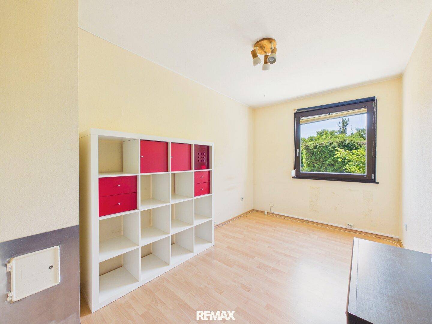 Helles Schlafzimmer mit Laminatboden und einem Fenster mit Blick ins Grüne.