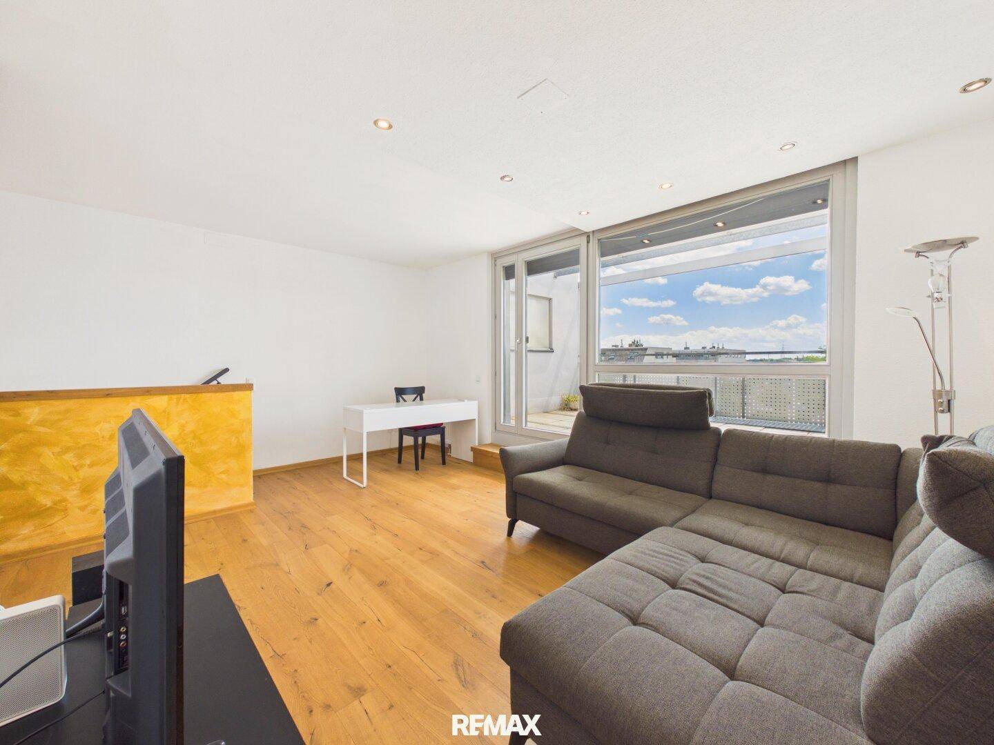 Helles Wohnzimmer mit Holzboden, großem Sofa und Zugang zu einer Terrasse mit Weitblick.
