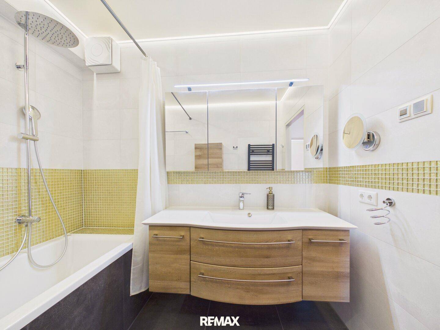 Modernes Badezimmer mit Badewanne, Dusche, elegantem Waschtisch und goldenen Mosaikfliesen.