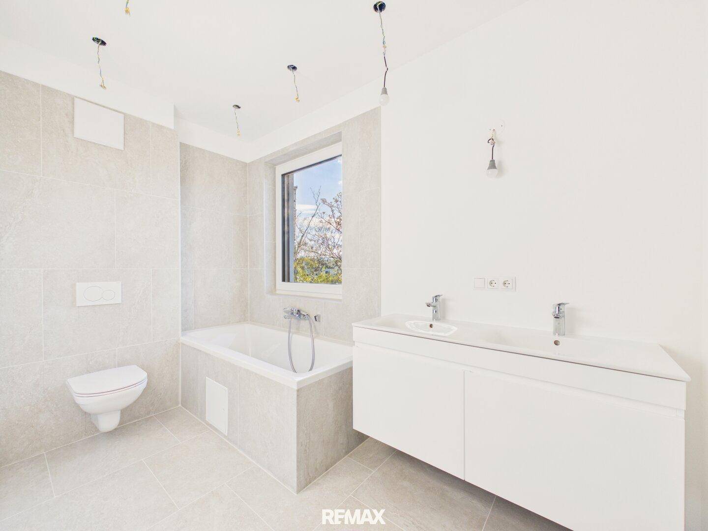 Geräumiges Badezimmer mit Badewanne, Doppelwaschbecken und Fenster, hell gefliest.