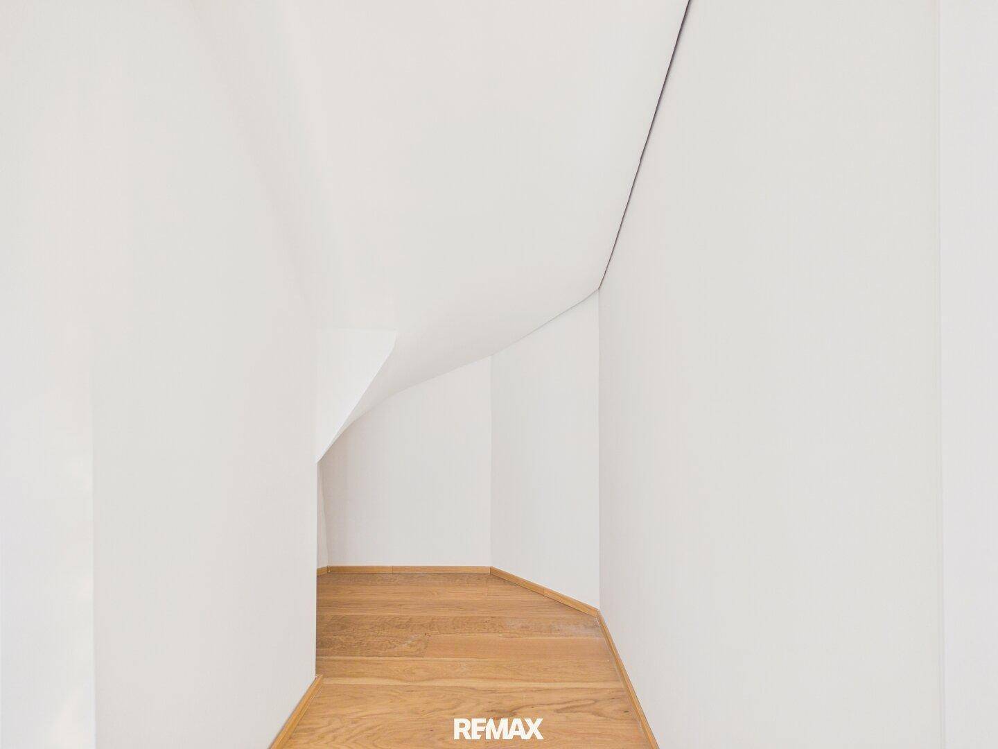 Heller Raumwinkel mit schrägen Wänden und Holzboden, möglicherweise unter einer Treppe.