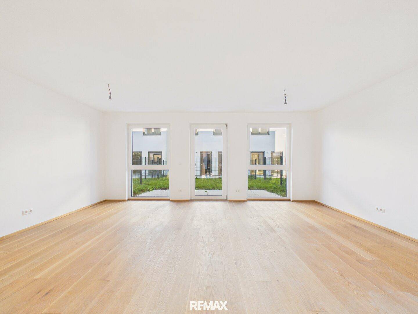 Geräumiges, helles Zimmer mit Holzboden und drei großen Fenstertüren zum Gartenbereich.