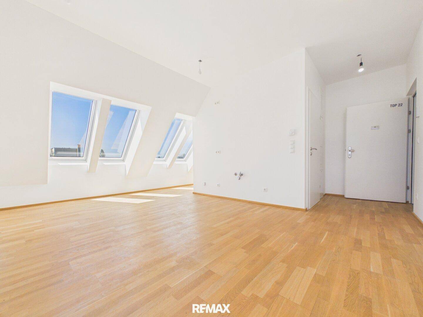 Heller Raum im Dachgeschoss mit Holzboden, Dachfenstern und Zugangstür.