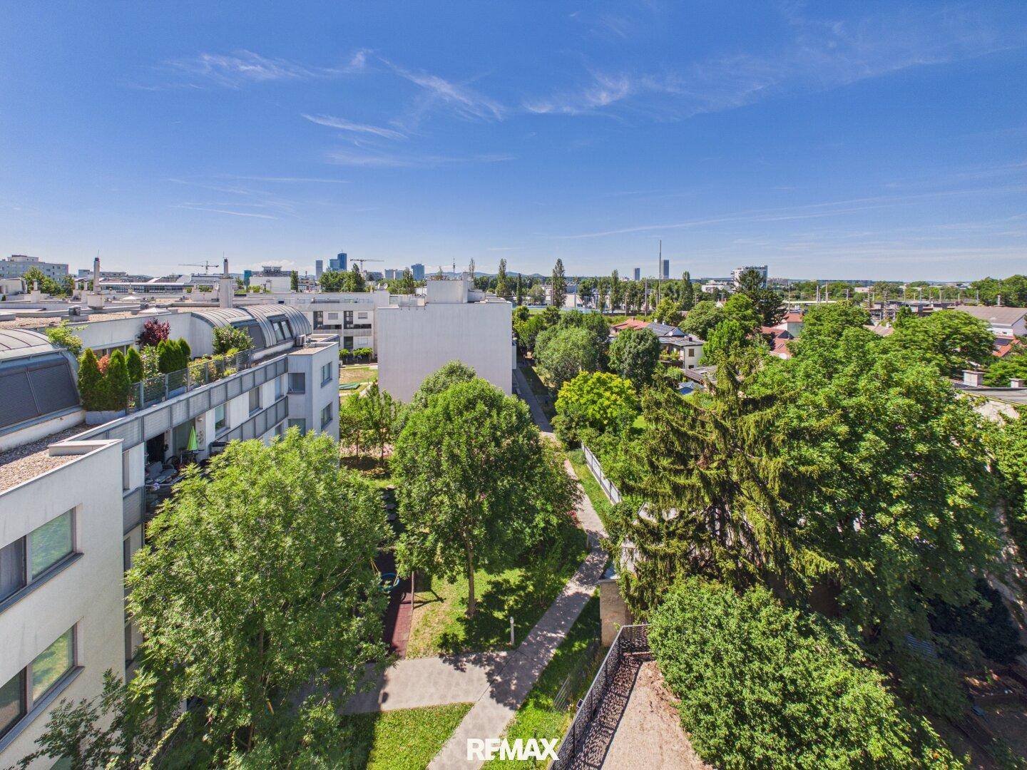 Weitläufiger Blick über eine grüne Wohngegend mit Bäumen und städtischer Skyline im Hintergrund.