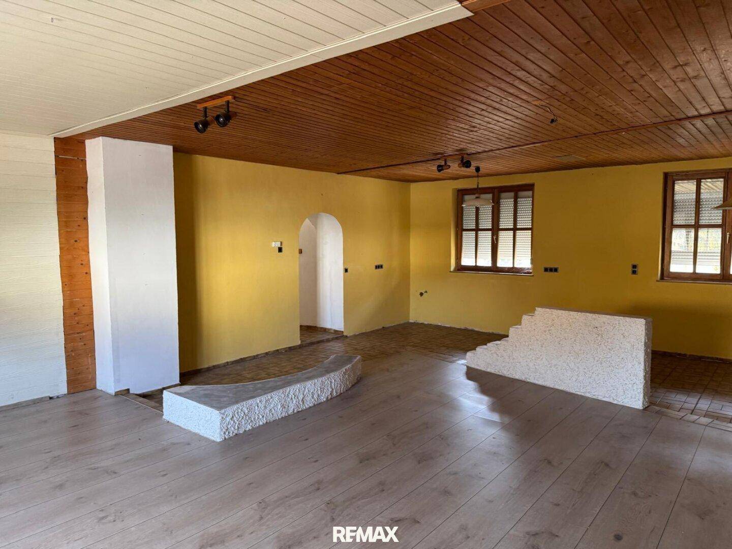 Geräumiger Raum mit Holzdecke, gelben Wänden und einer Mischung aus Holz- und Laminatboden.