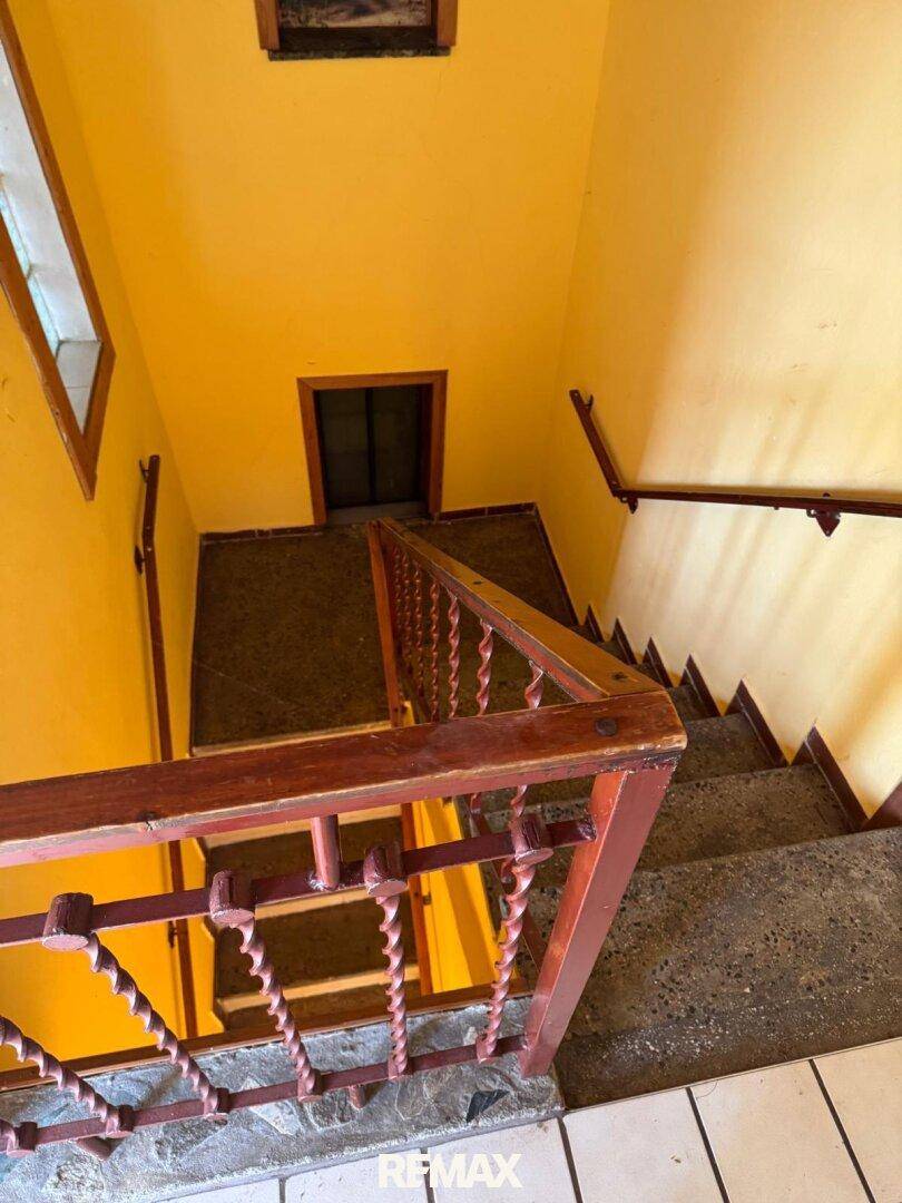 Treppenhaus mit gelben Wänden und einem Holzgeländer, das in die untere Etage führt.