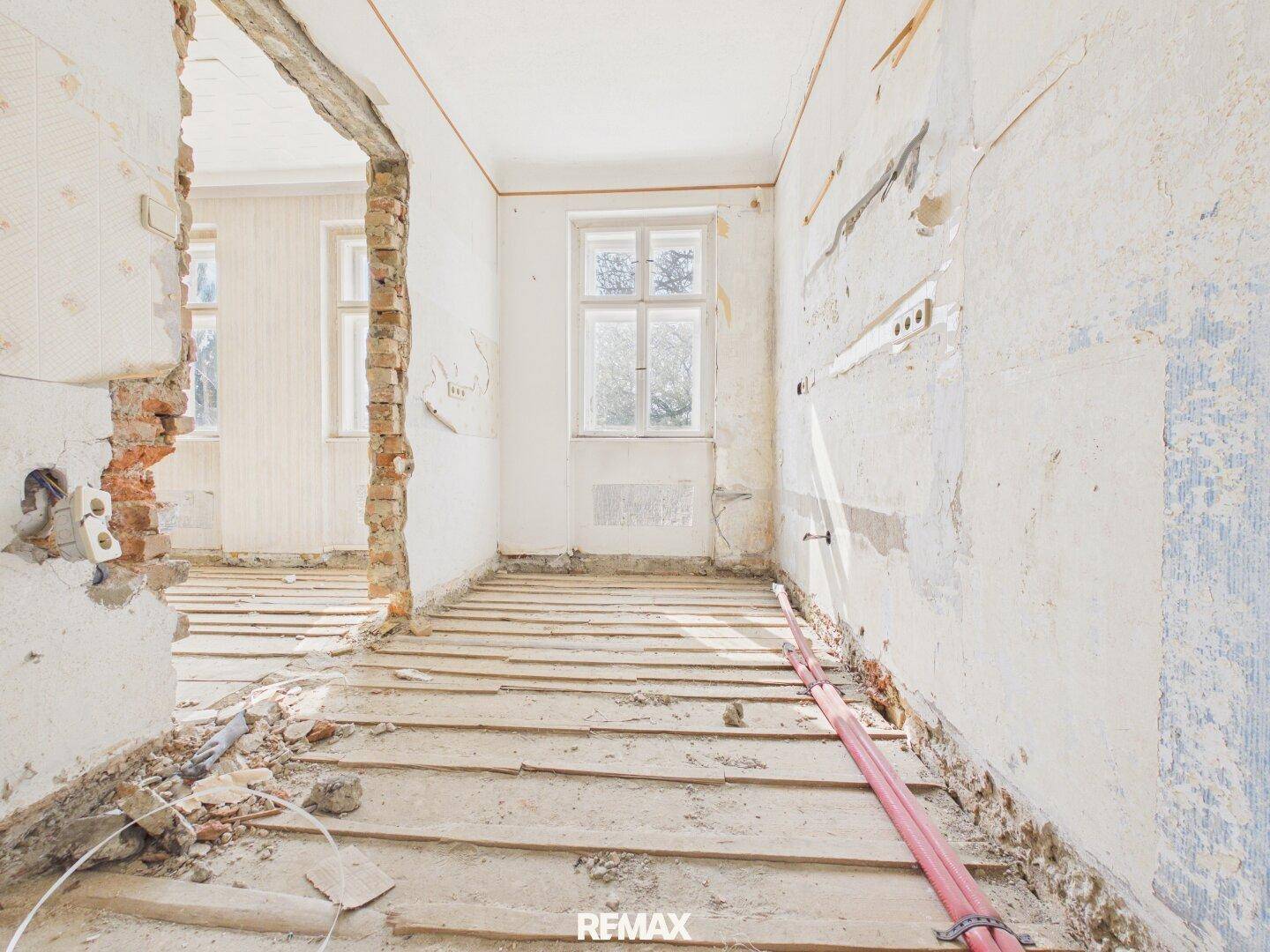 Durchgangsraum im Rohbau mit freigelegten Holzdielen und Blick auf weitere Zimmer.