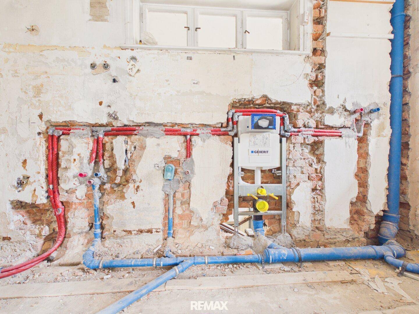 Badezimmer im Rohbau mit sichtbaren Wasserleitungen und Vorinstallation für die Toilette.