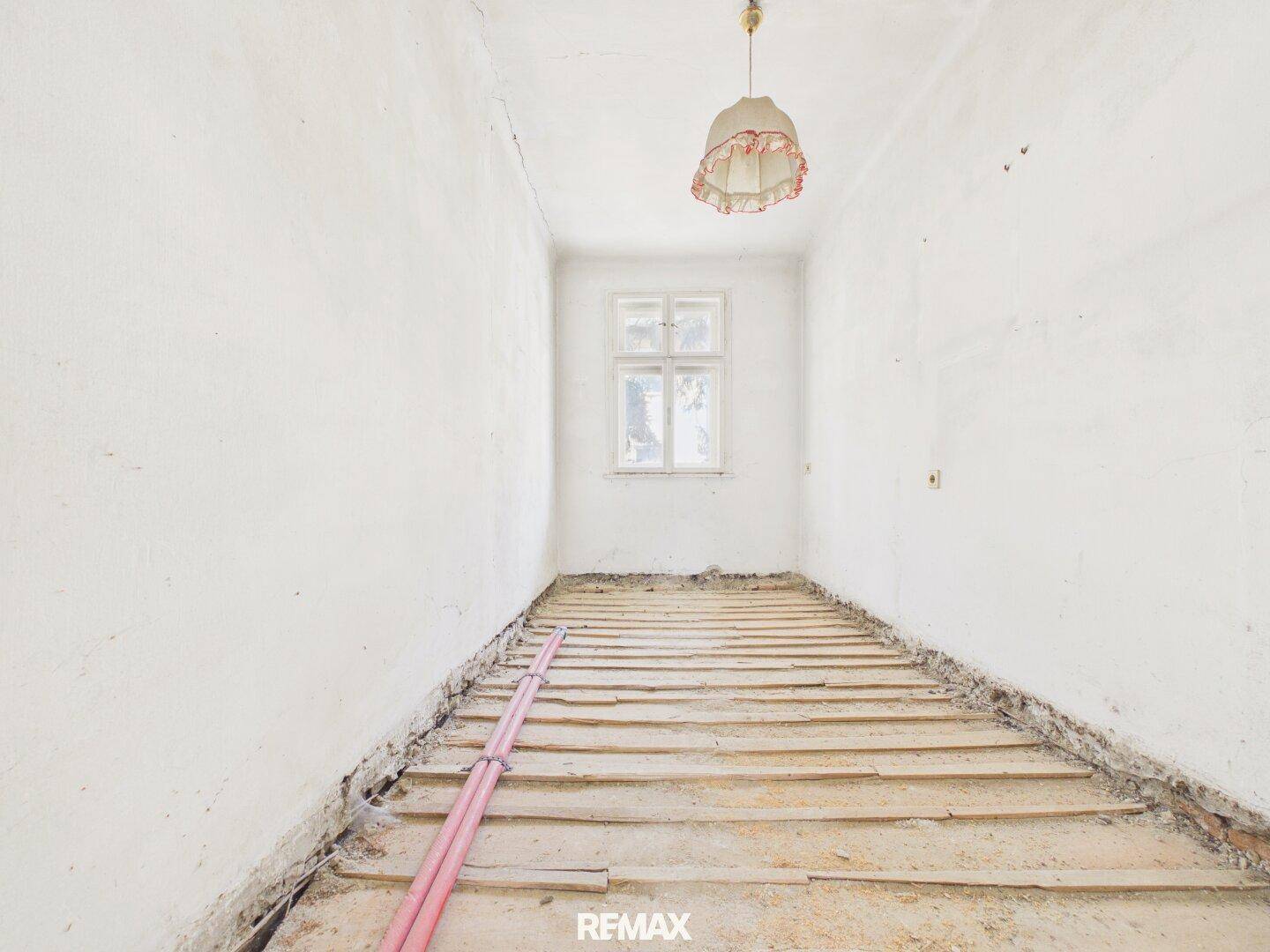 Kleiner Raum im Rohbau mit einem Fenster und freigelegten Holzdielen, bereit zur Gestaltung.