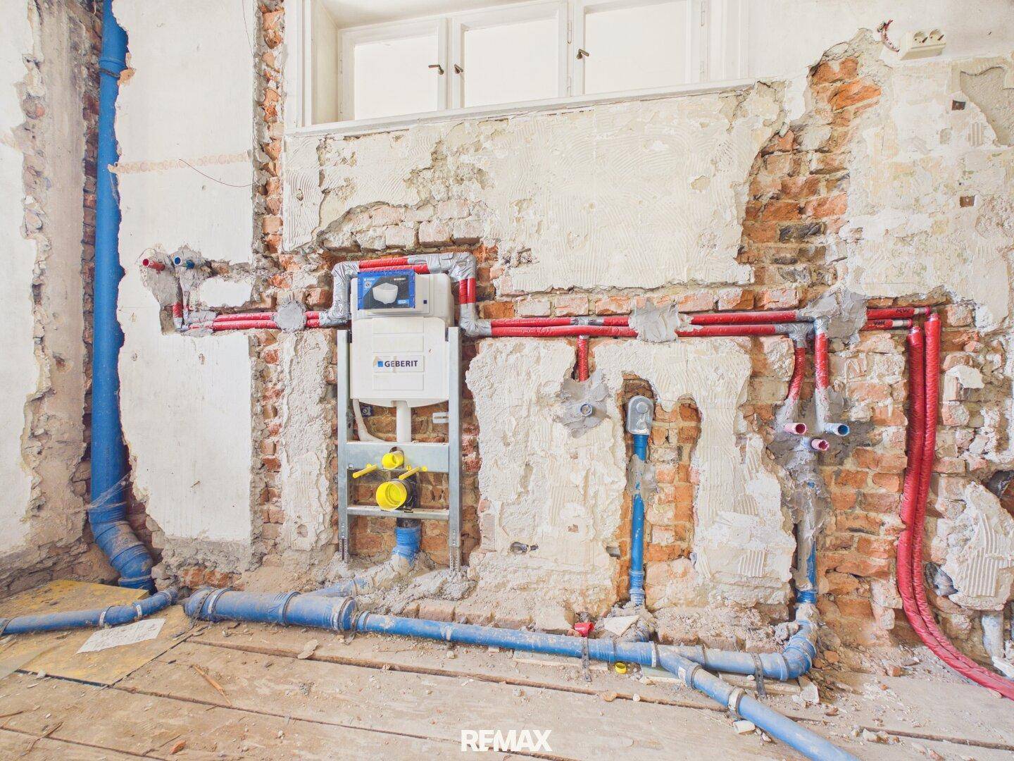 Badezimmer im Rohbau mit sichtbaren Wasserleitungen und Vorinstallation für die Toilette.