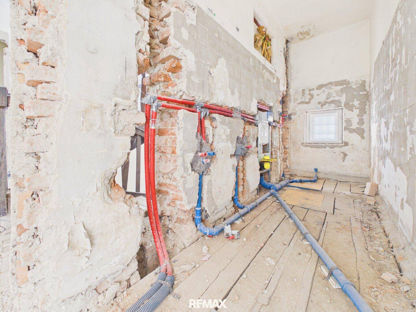 Badezimmer im Rohbau mit sichtbaren Wasserleitungen und Vorinstallation für die Toilette.