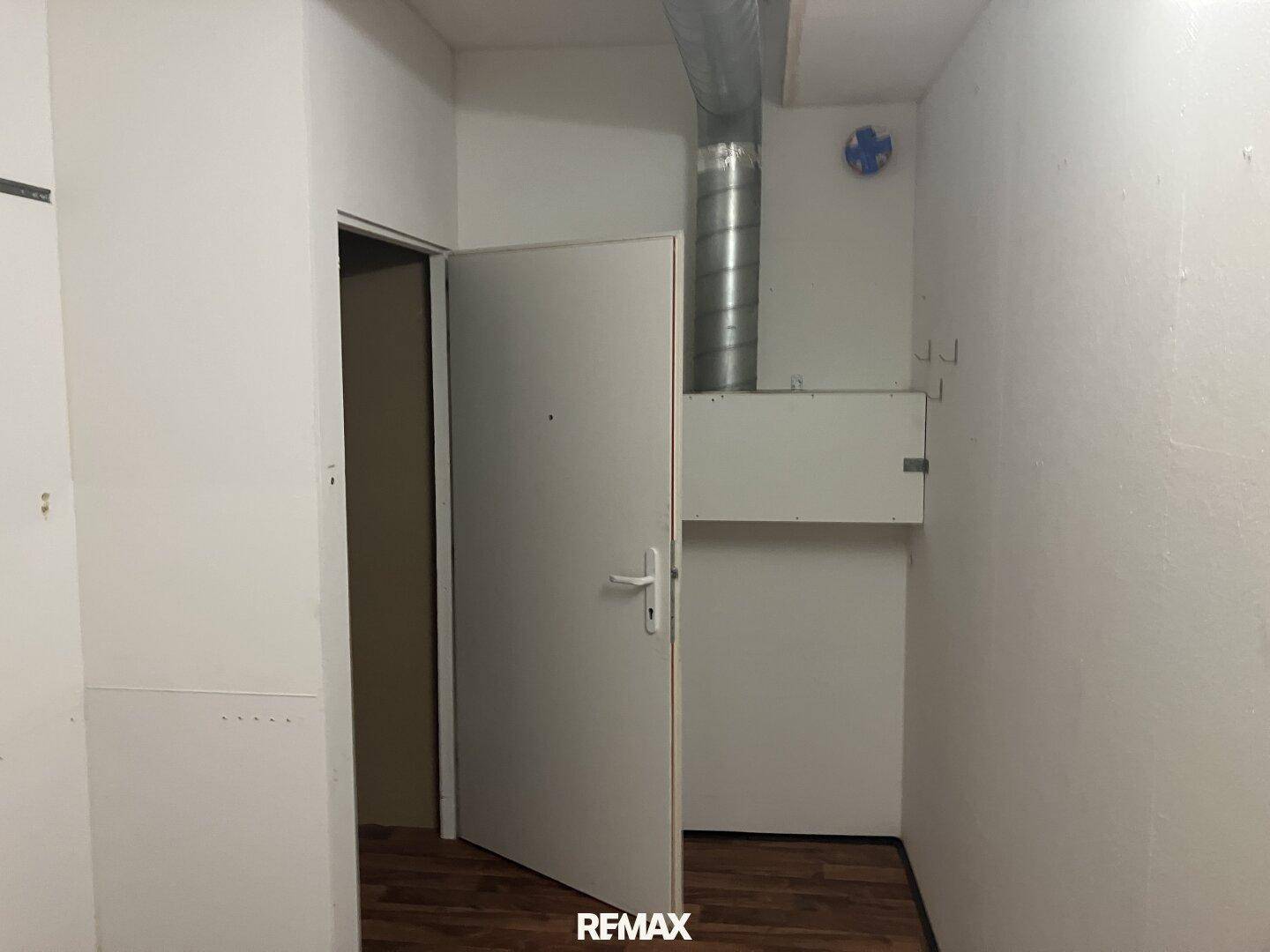 Kleiner Technikraum mit offener Tür und sichtbarer Lüftungsleitung an der Decke und Laminatboden.