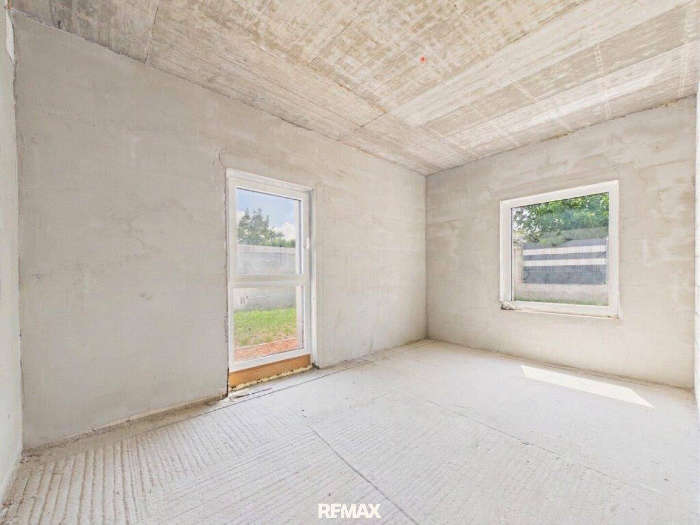 Unfertiger Raum mit Betondecke und Fenster, das den Blick ins Grüne freigibt.
