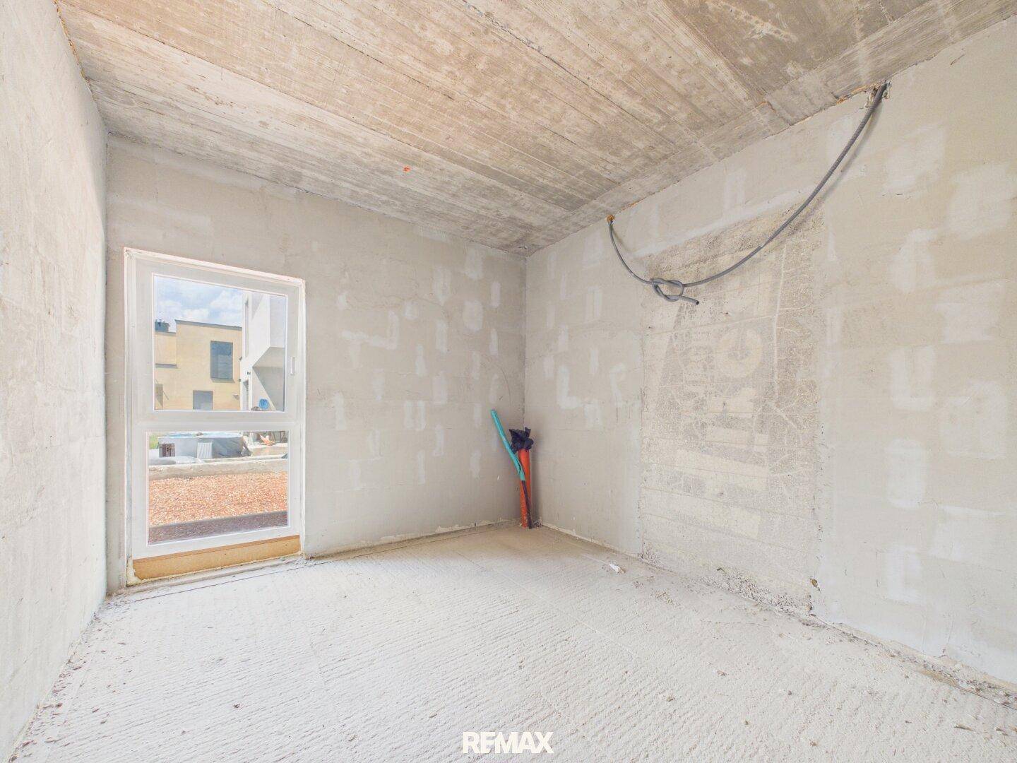 Unfertiger Raum mit Betondecke und Zugang nach draußen, bereit für den Innenausbau.