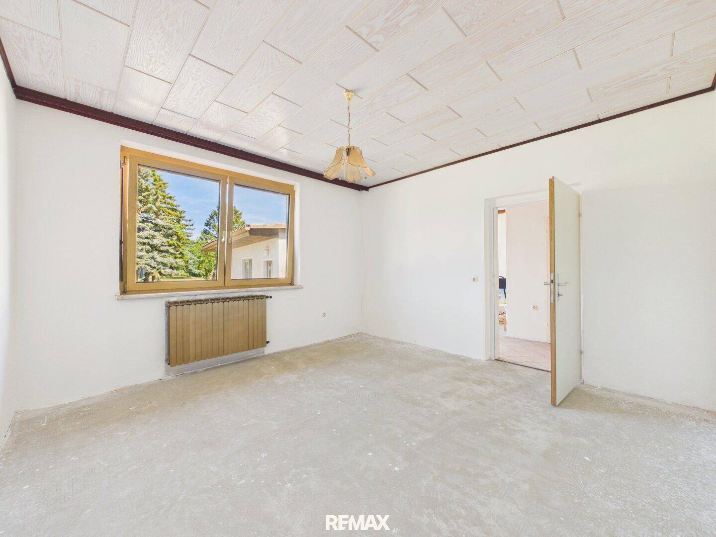 Leerer Raum mit Holzpaneeldecke und großem Fenster, bereit für Renovierung.