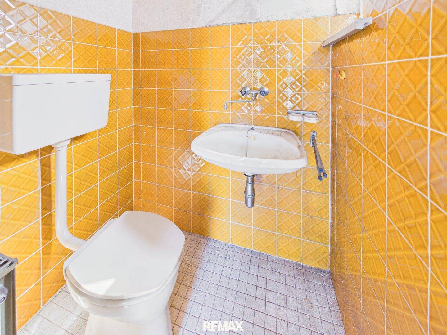 Badezimmer mit gelben Fliesen, Waschbecken und Toilette, im Stil der 80er Jahre.