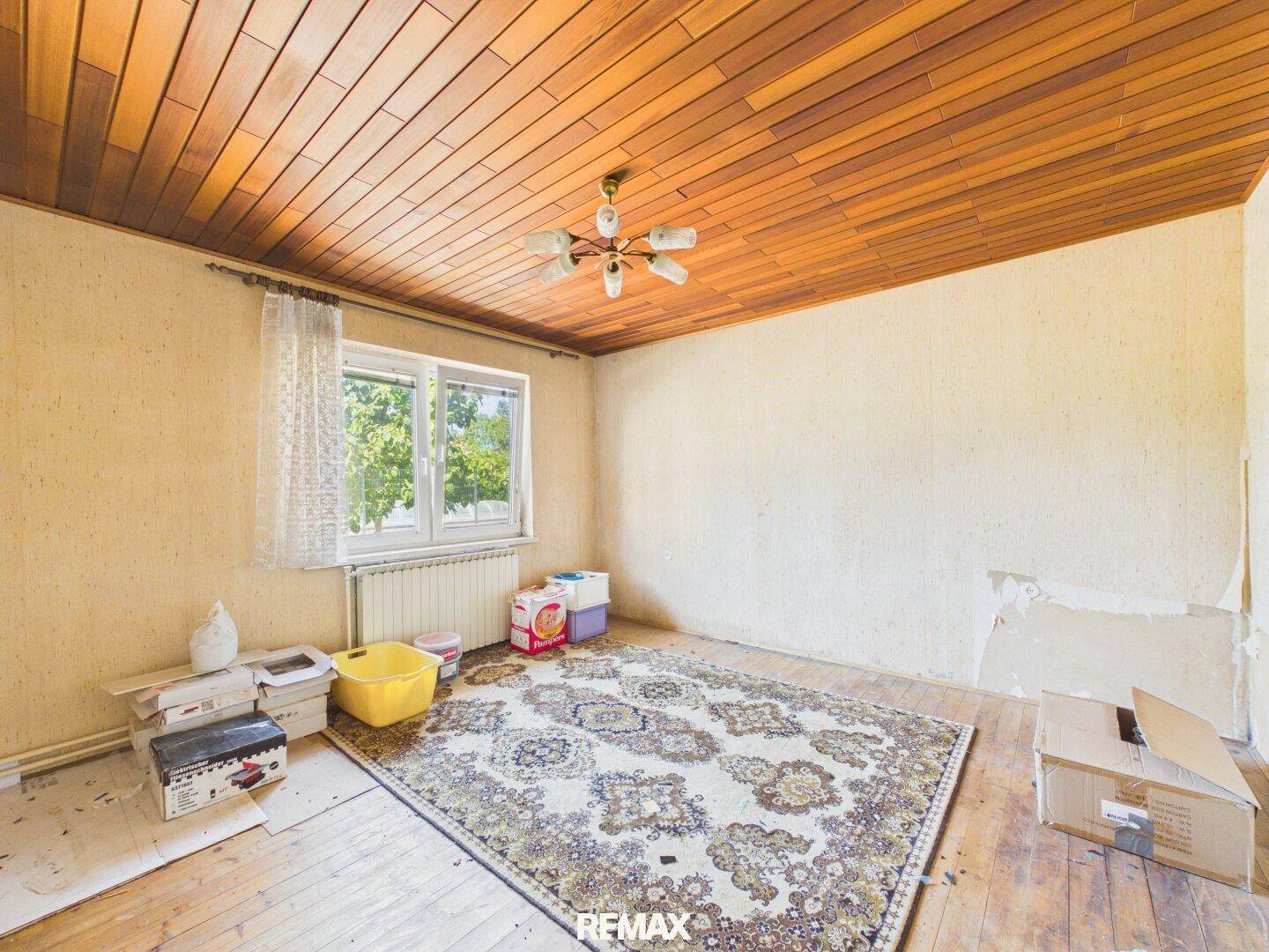 Renovierungsbedürftiger Raum mit Holzpaneeldecke, Teppich und Fenster.