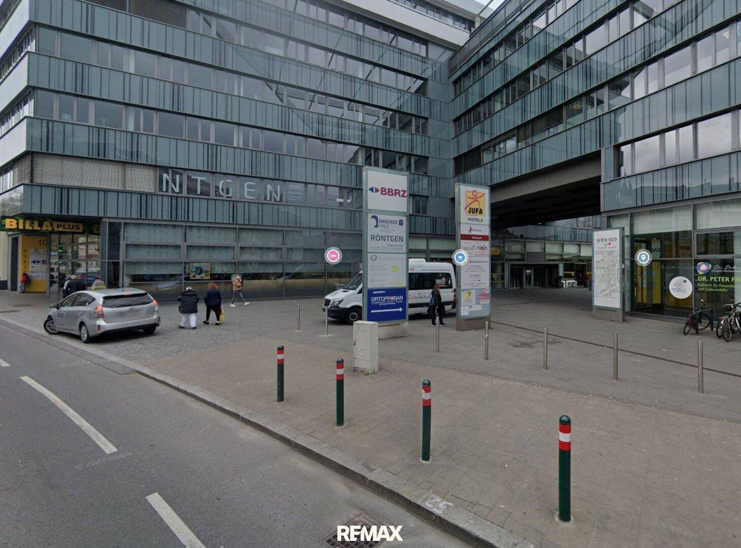 Modernes Geschäftsgebäude mit Glasfassade, umgeben von einer Straße und verschiedenen Werbeschildern.