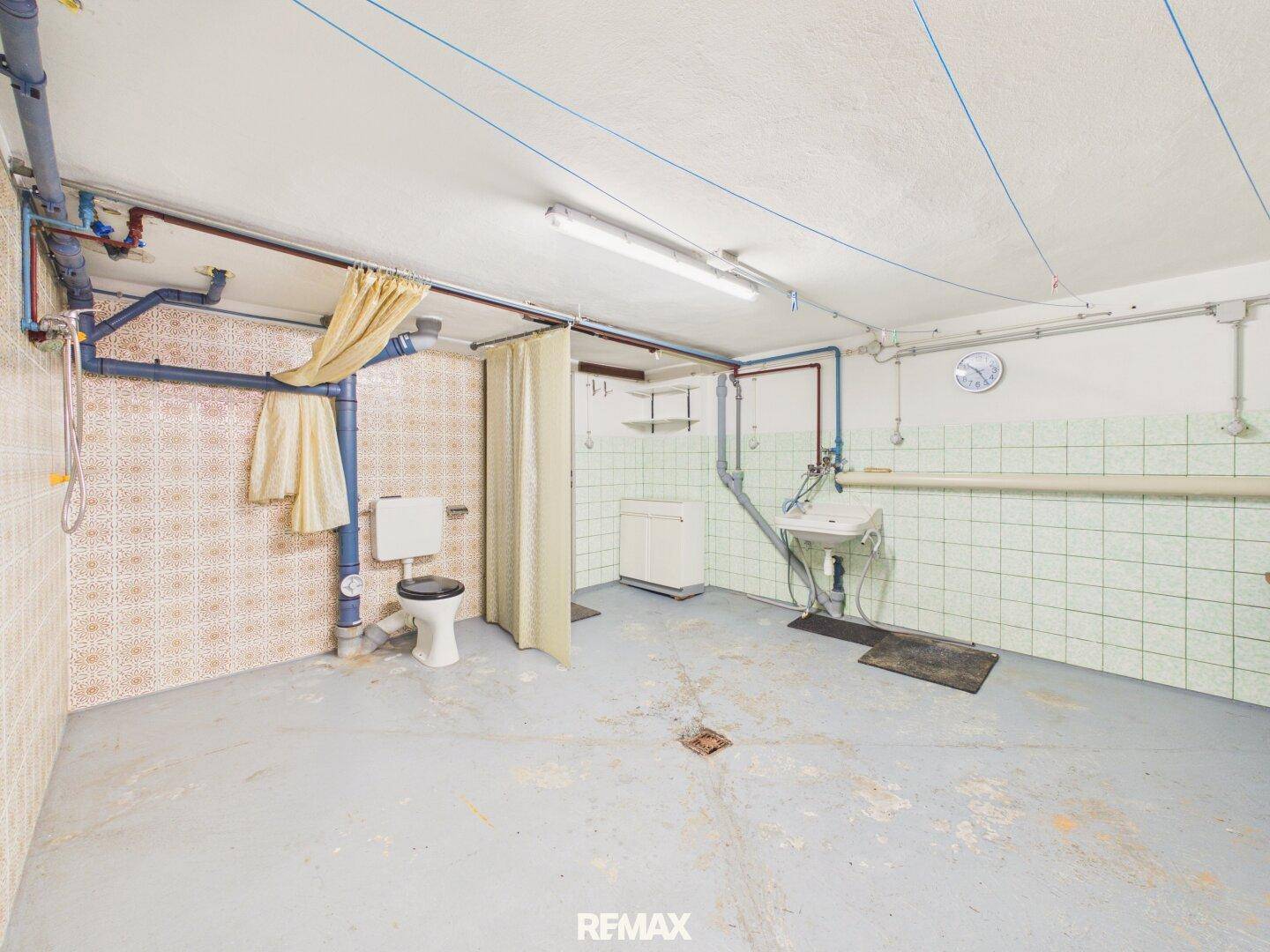 Waschraum im Keller mit Toilette, Waschbecken und Duschvorhang, funktional eingerichtet.