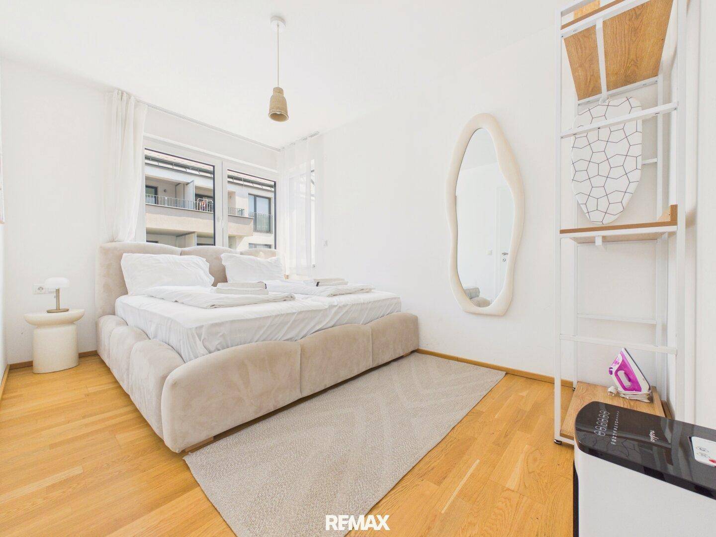 Gemütliches Schlafzimmer mit großem Doppelbett, modernem Spiegel und hellem Holzboden.