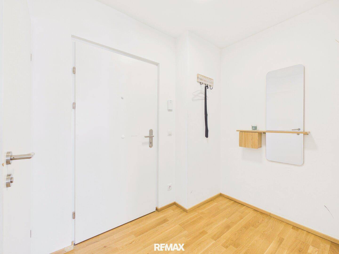 Heller Eingangsbereich mit Holzboden, Garderobe und einem praktischen Wandspiegel.