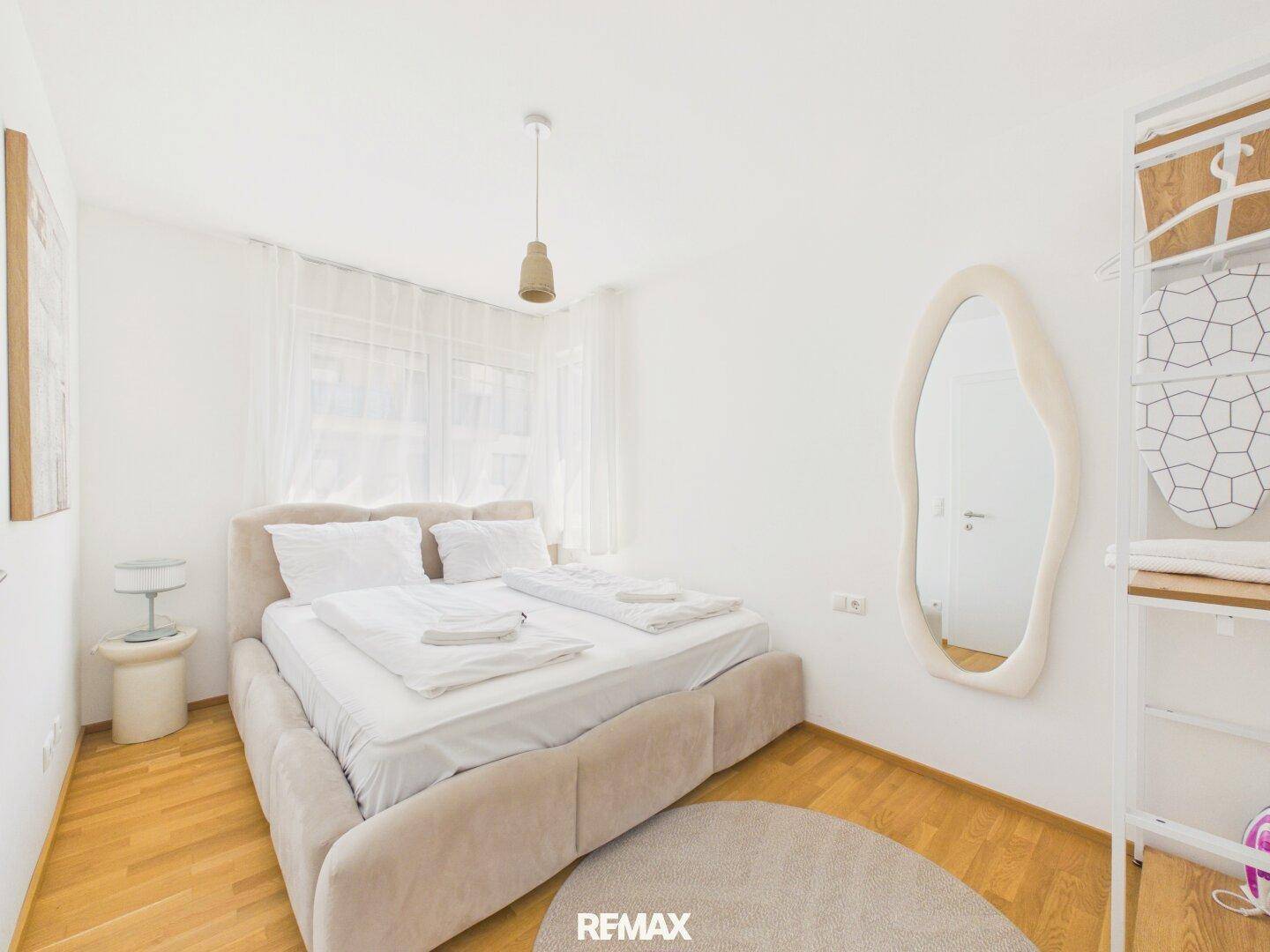 Helles Schlafzimmer mit Doppelbett, Holzboden und einem großen, modernen Spiegel.